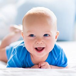 baby smiling on his stomach in a blue shirt